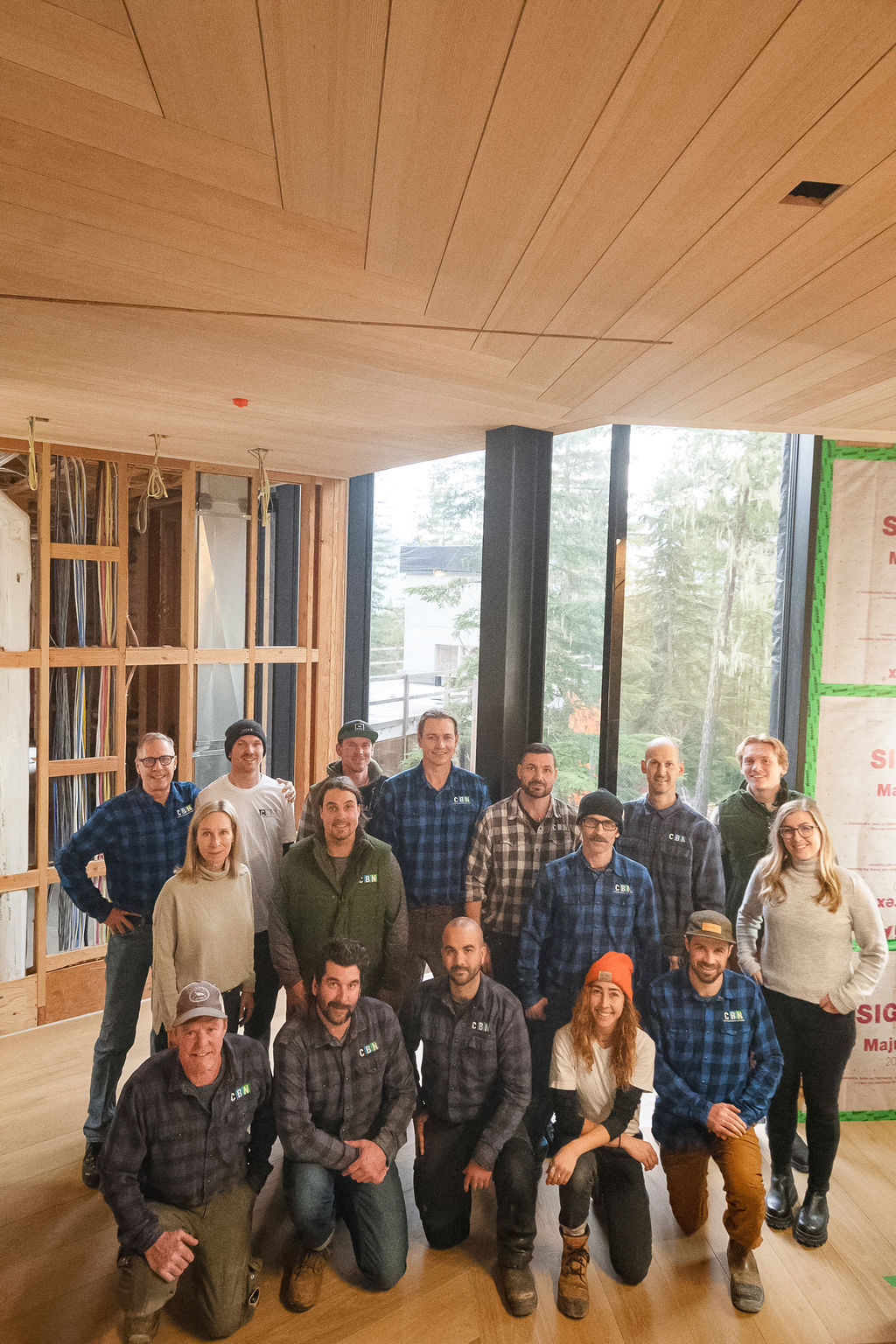 A group of fifteen people pose for a photo inside a modern Custom Building Network facility under construction, featuring floor-to-ceiling windows and exposed wiring.