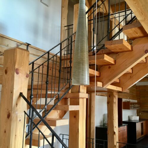 A wooden staircase with black metal railings is shown inside a modern, rustic interior featuring exposed beams and wood paneling.