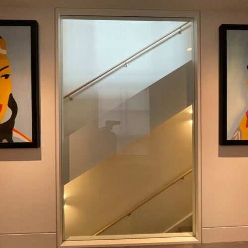A hallway with a glass window overlooking a stairwell, flanked by two framed portraits of individuals in Native American attire on either side.