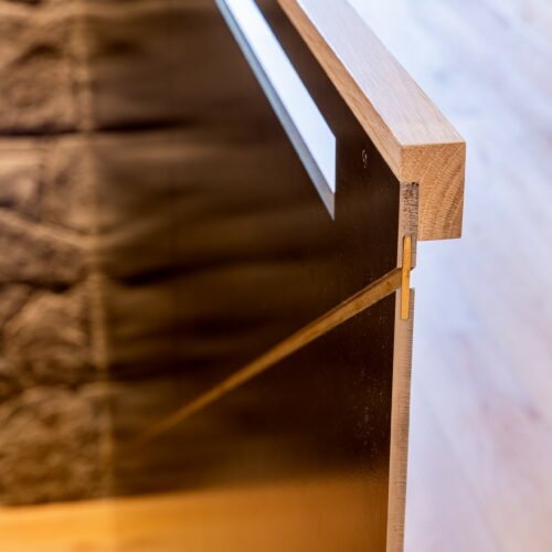 Close-up of a modern wooden and glass railing with metal support on a light-colored wood floor and stone wall background.