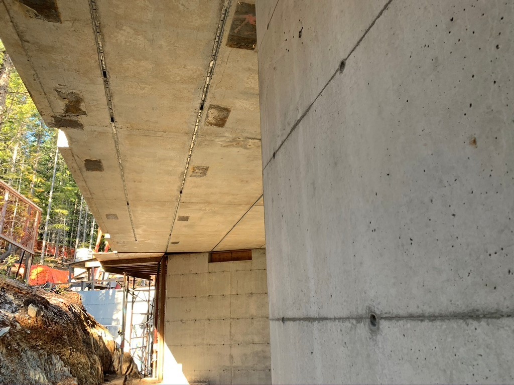 A concrete building under construction with visible ceiling, walls, support scaffolding, and exposed construction materials. Sunlight illuminates part of the site.