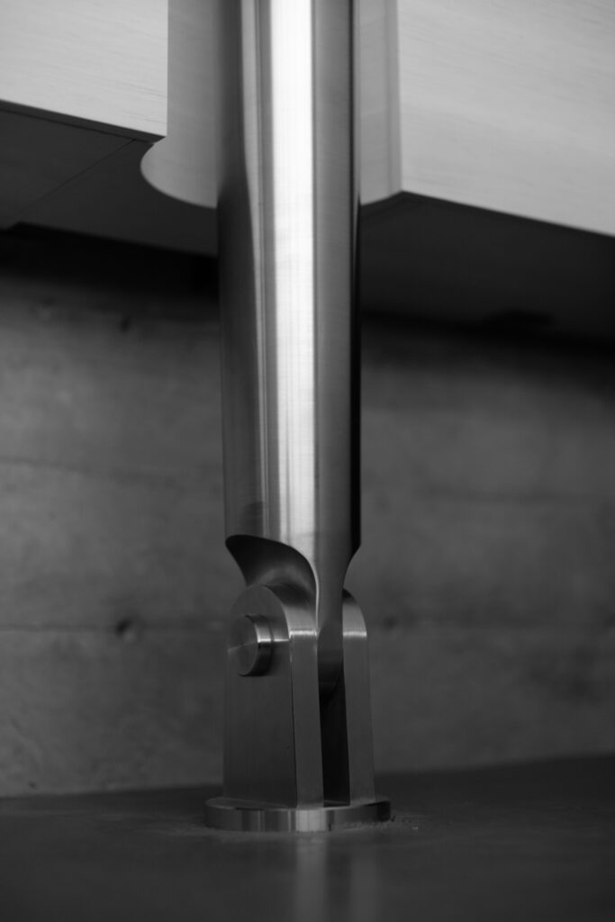 A close-up view of a metallic cylindrical support column attached to a surface, shown in black and white.