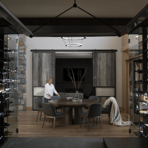 A person stands near a round dining table set for four in a modern room, with wine racks on both sides and rustic sliding barn doors in the background.